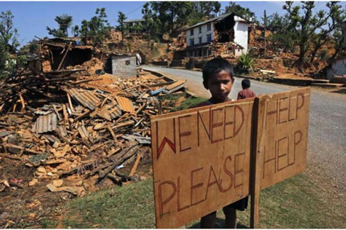 ငလျင်ကြောင့် ပျက်စီးသွားသည့်ရွာမှ ကလေးတစ်ဦး အကူအညီတောင်းခံသော ဆိုင်းဘုတ်နောက်တွင် ရပ်နေစဉ်။ (ဓာတ်ပုံ - အေပီ)
