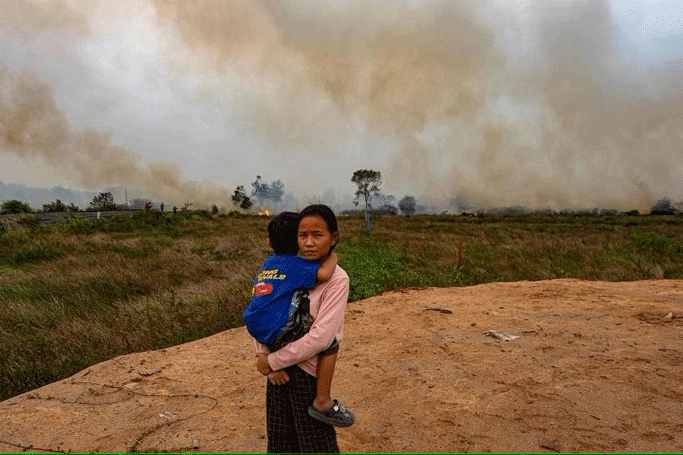 Photo - AFP (ဆူမားတြားတောင်ပိုင်းရှိ သူမ၏အိမ်အနီးတွင် မီးငြှိမ်းသတ်ရန် ကြိုးစားနေစဉ် မောင်ဖြစ်သူကို သယ်ဆောင်လာသည့် မိန်းကလေးတစ်ဦး၊)