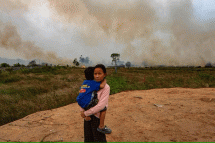 Photo - AFP (ဆူမားတြားတောင်ပိုင်းရှိ သူမ၏အိမ်အနီးတွင် မီးငြှိမ်းသတ်ရန် ကြိုးစားနေစဉ် မောင်ဖြစ်သူကို သယ်ဆောင်လာသည့် မိန်းကလေးတစ်ဦး၊)